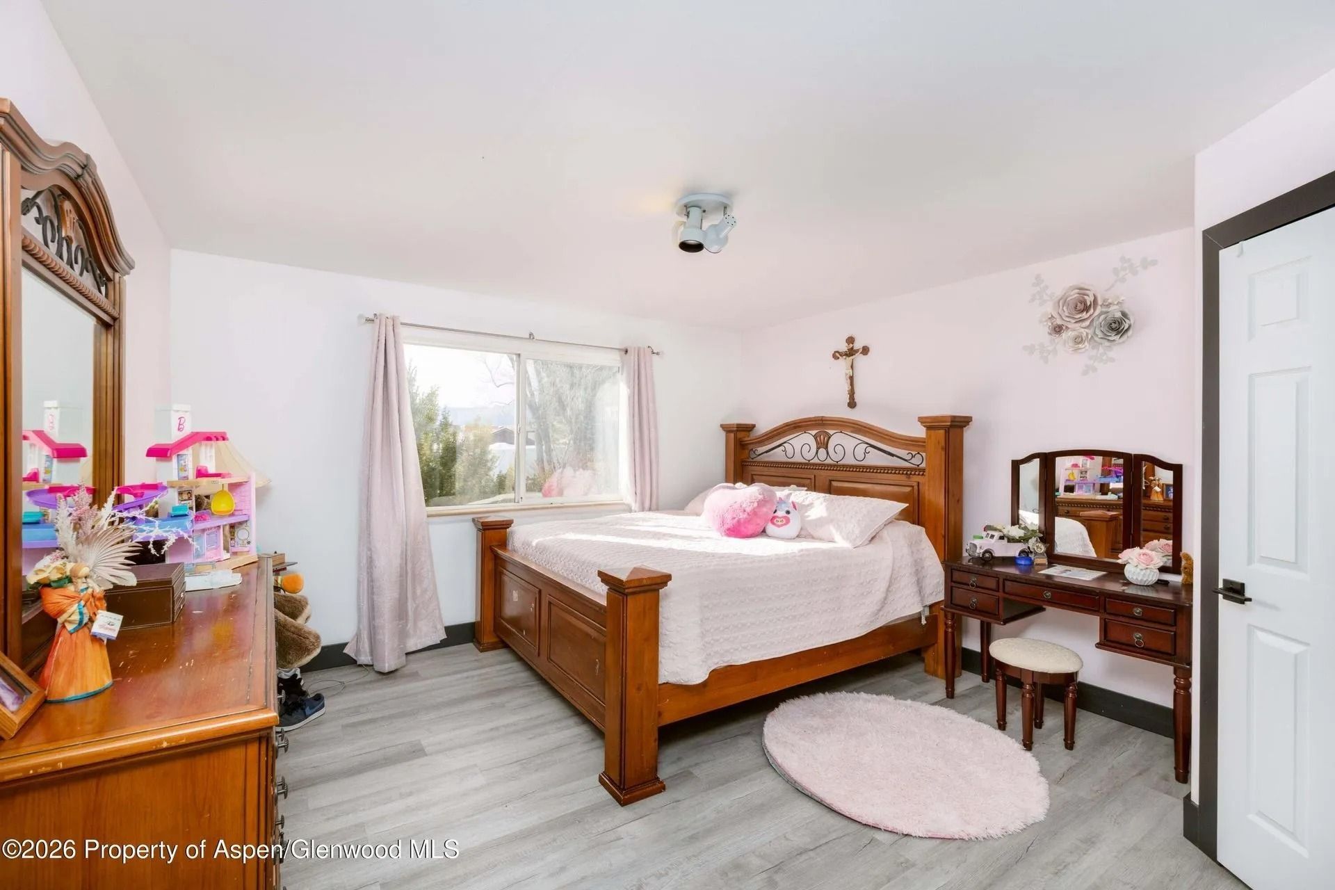 Bedroom with wooden bed, vanity, dresser, and window with curtains in a bright white room