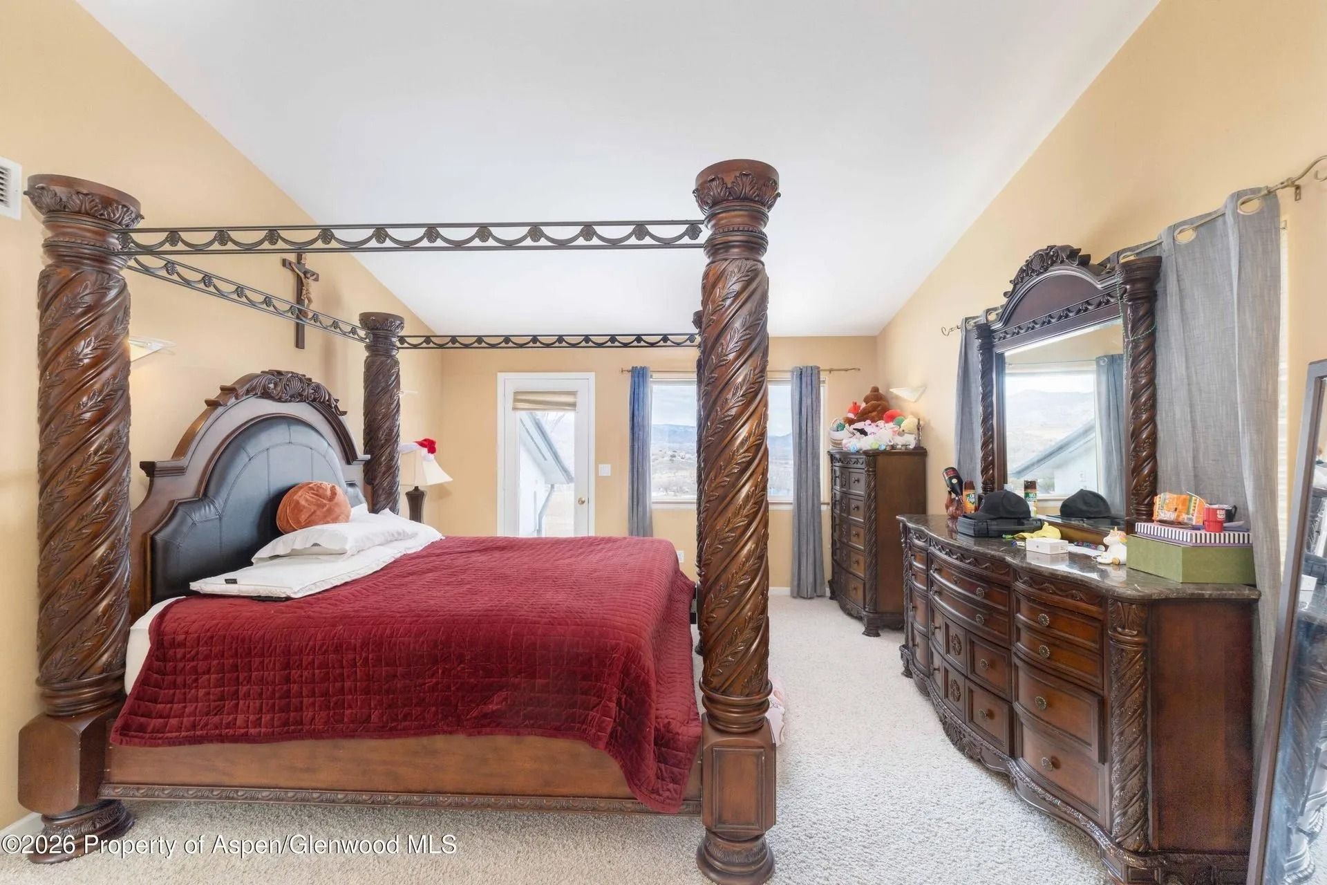 Bedroom with four-poster bed, ornate dresser, and mirror in a bright, carpeted room