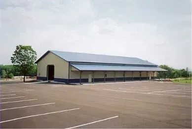 Large, rectangular building with blue roof and awning, beige walls, and empty parking lot. Large, rectangular building with blue roof and awning, beige walls, and empty parking lot.