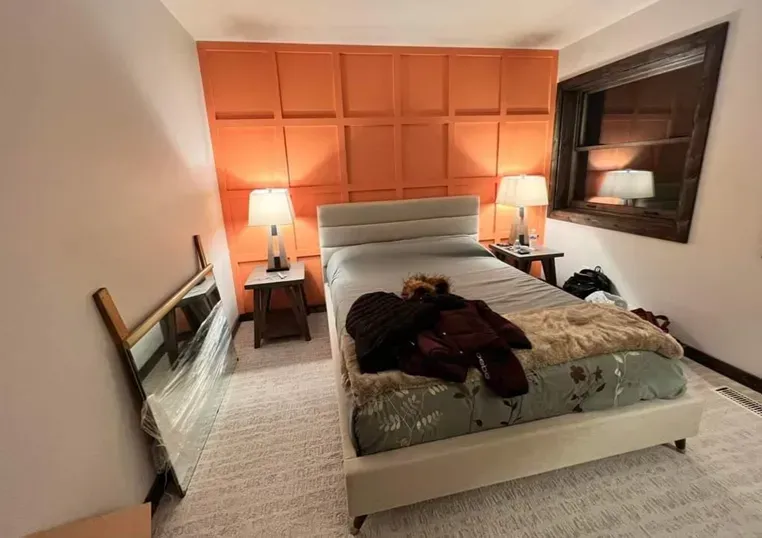 Orange textured wall behind a bed, flanked by tables with lamps; mirror leaning against a wall.