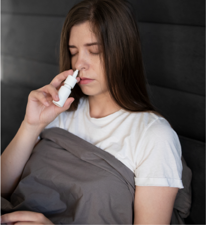 Una mujer está acostada en la cama usando un aerosol nasal.