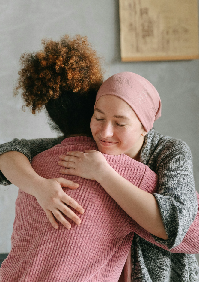 Una mujer con cáncer abraza a otra mujer con un suéter rosa.