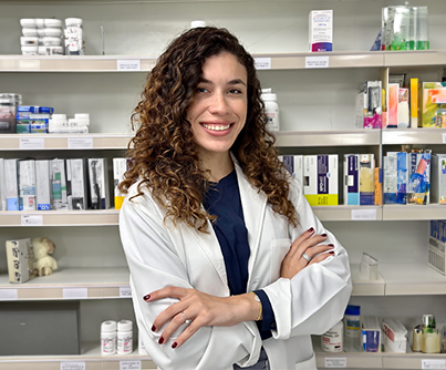 Una mujer con bata de laboratorio está parada frente a un estante de una farmacia.