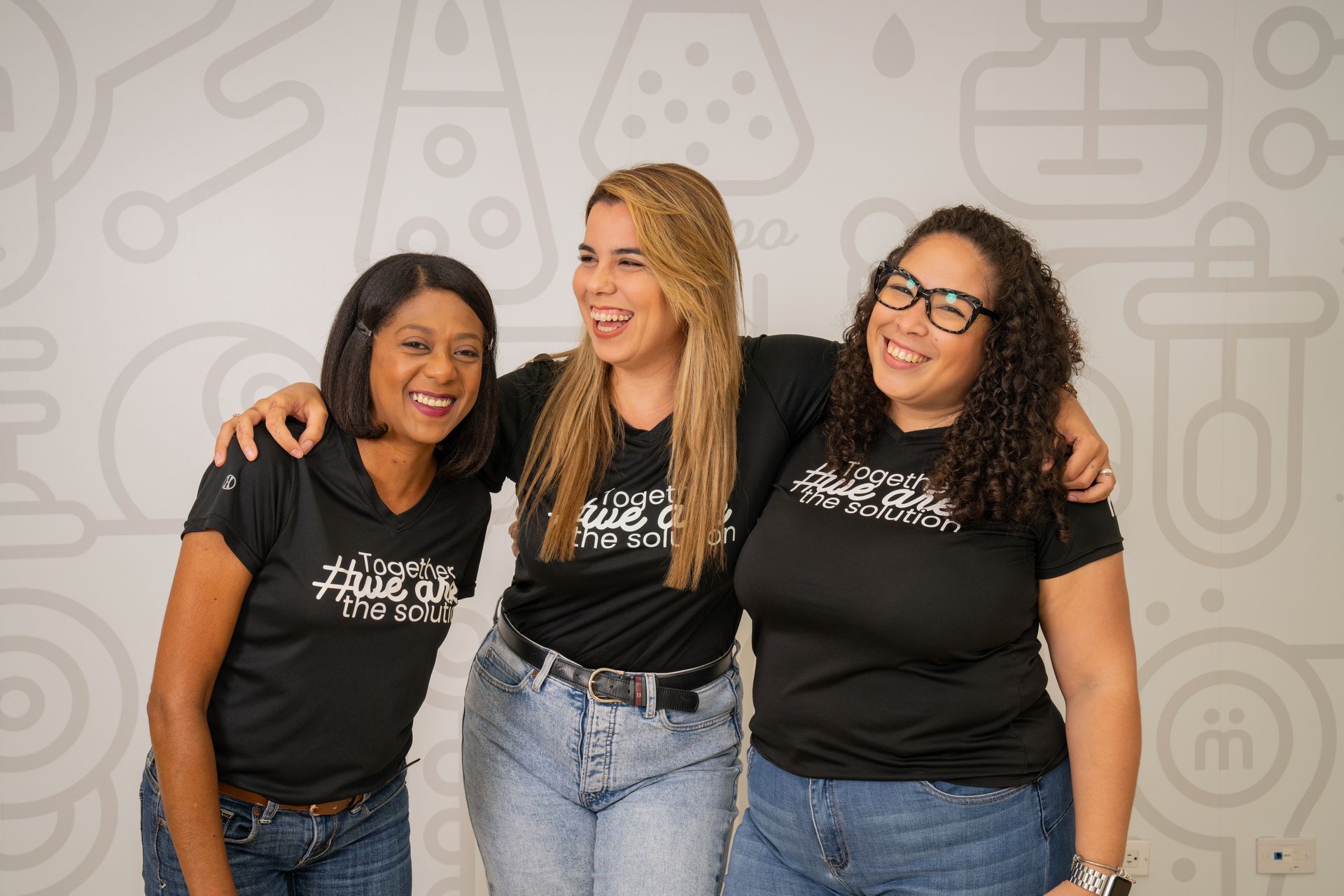 Tres mujeres posan juntas para una fotografía mientras visten camisas negras.