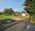 Chain-link fence overlooking a small pond, grassy yard, and white house under a blue sky
