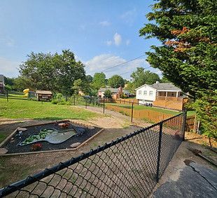 Chain-link fence overlooking a small pond, grassy yard, and white house under a blue sky