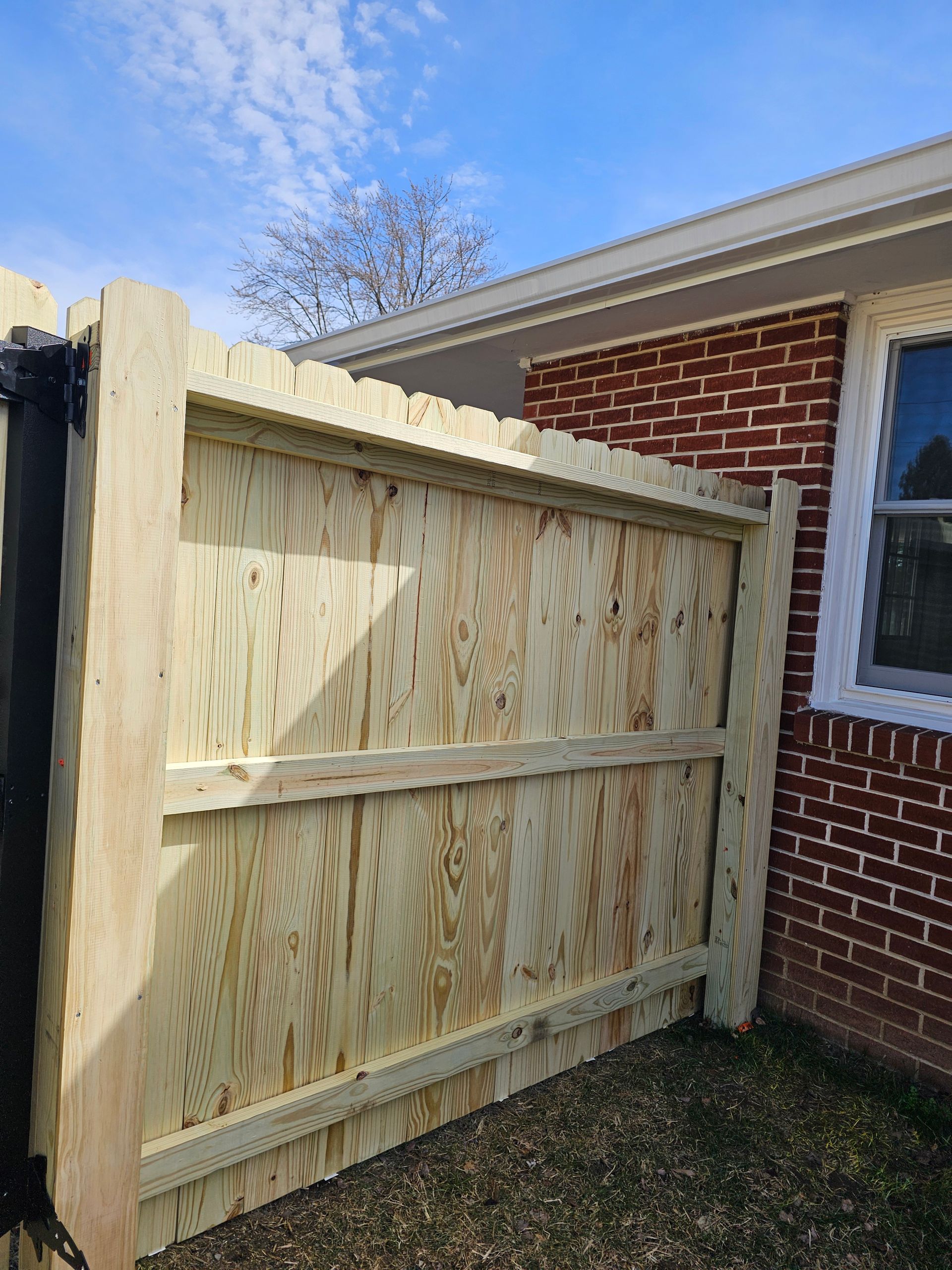 New wooden fence beside a red brick house under a blue sky