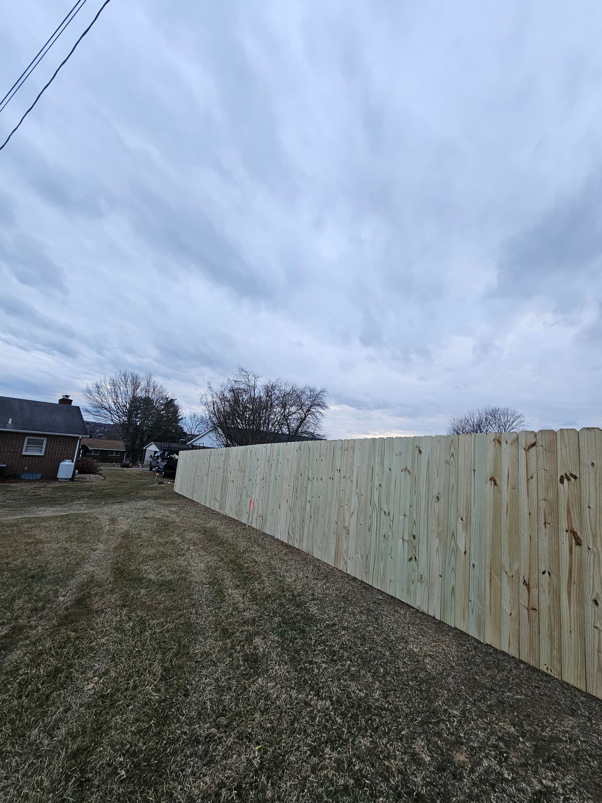 Grassy field beside a pale wooden fence under a cloudy sky