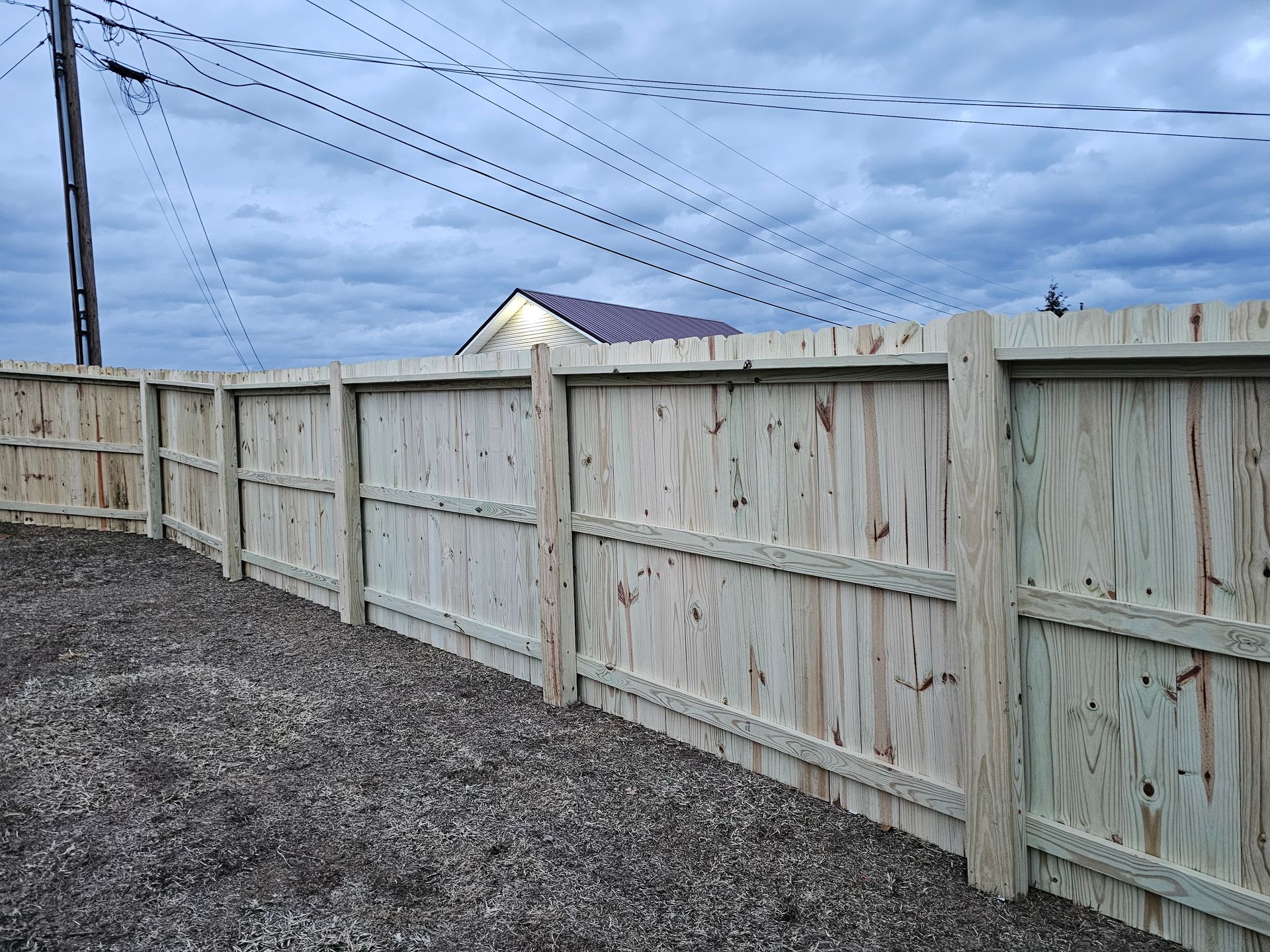 Tall wooden fence bordering a gravel yard under a cloudy sky
