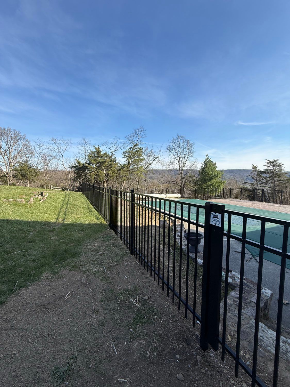 Black metal fence beside a grassy yard and outdoor pool under a clear blue sky