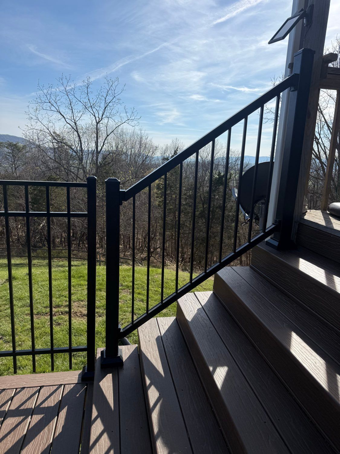 Black metal stair railing beside outdoor steps, with a grassy yard and blue sky in the background