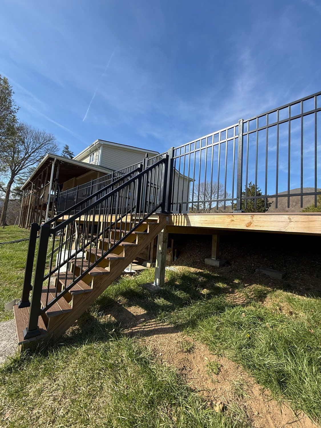 Outdoor wooden staircase leading to a raised deck with black metal railing under a blue sky