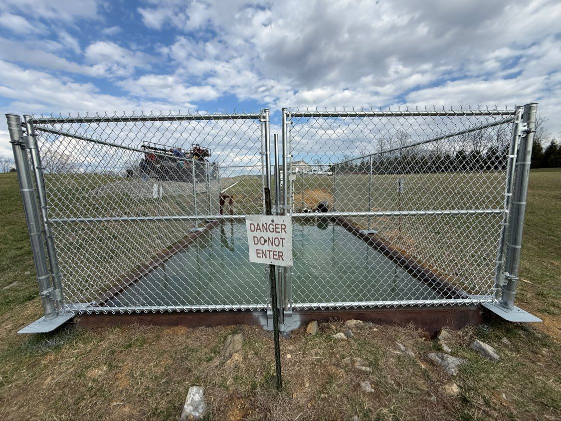 Chain-link gate blocking a road, with a warning sign at the center