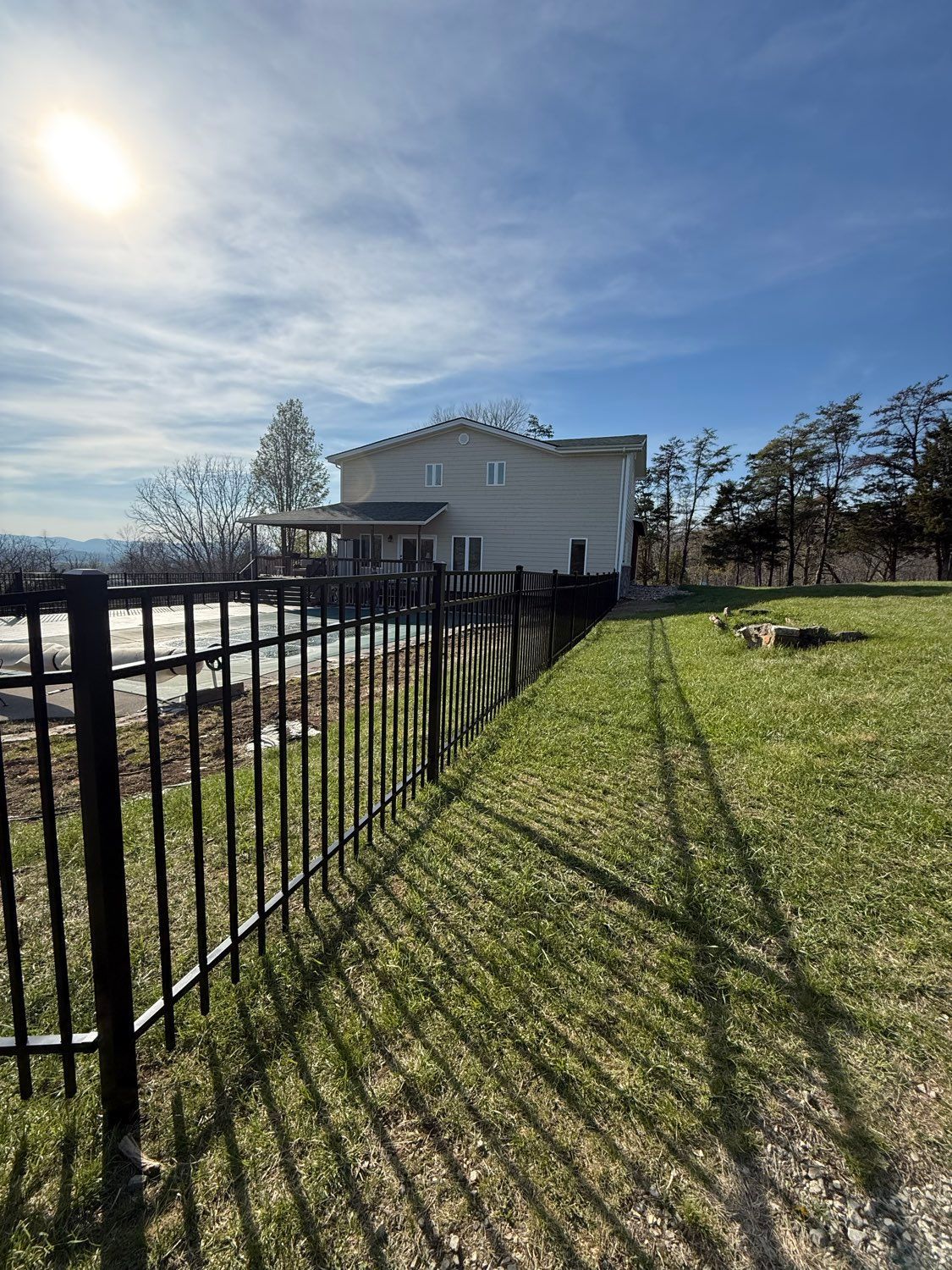 Sunny backyard with black metal fence, green lawn, and a white house by the water.