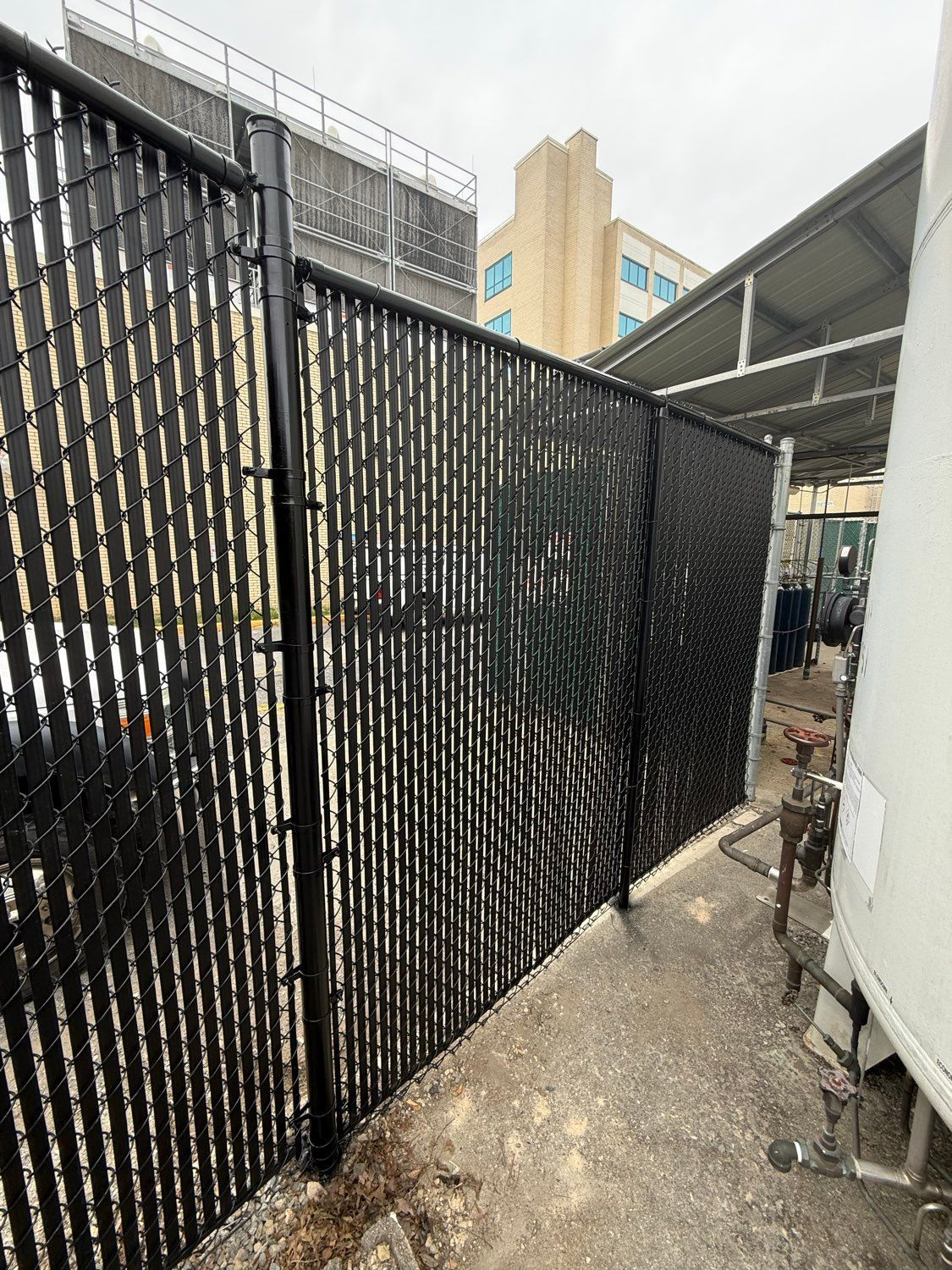 Black chain-link fence beside a white building in a narrow outdoor alley