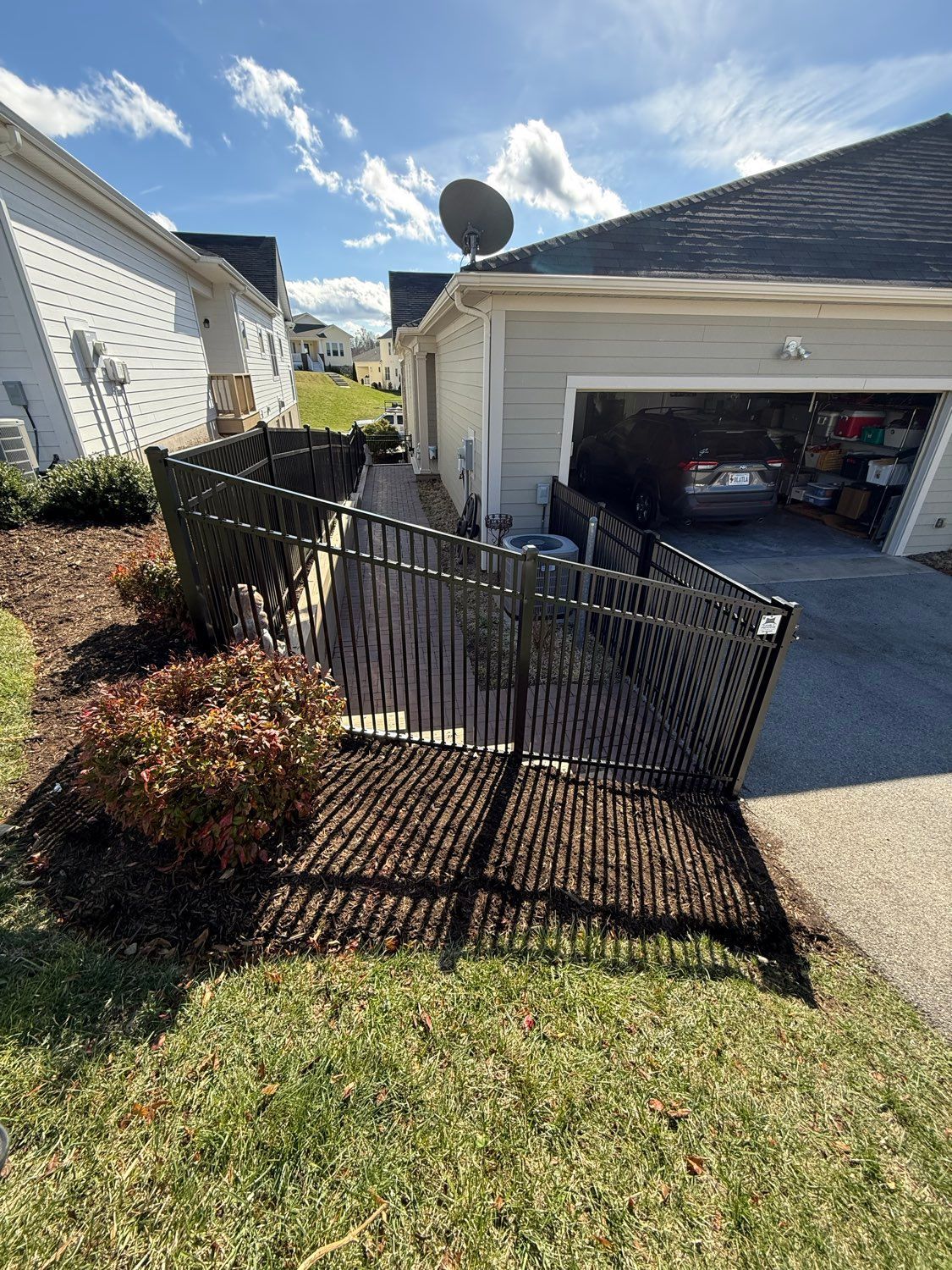 Bent black fence bent around a sloped front yard beside a garage driveway under a sunny sky