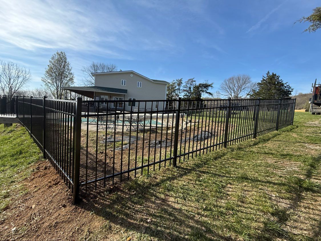 Black metal fence enclosing a yard beside a white house under a blue sky