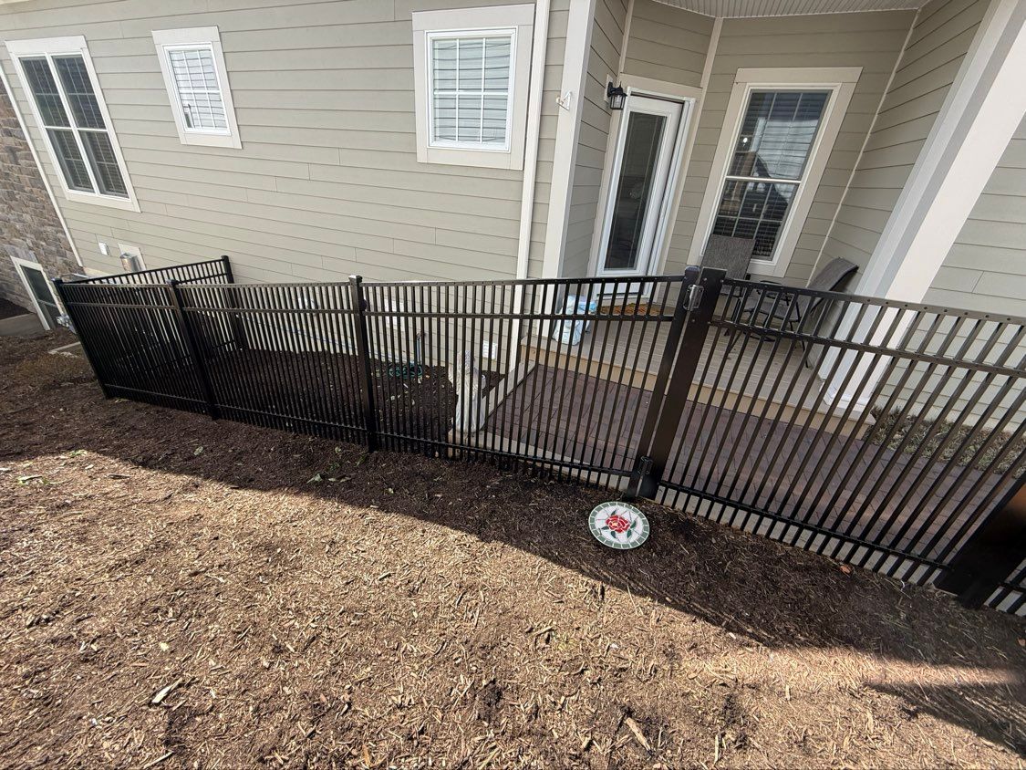 Black metal fence enclosing a small patio beside a beige house with white-trimmed windows and doors