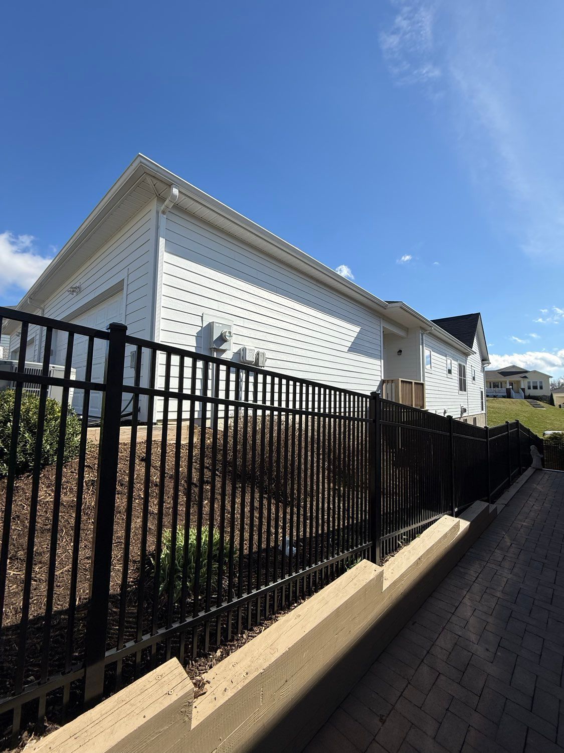White house with black fence along a brick walkway under a blue sky.