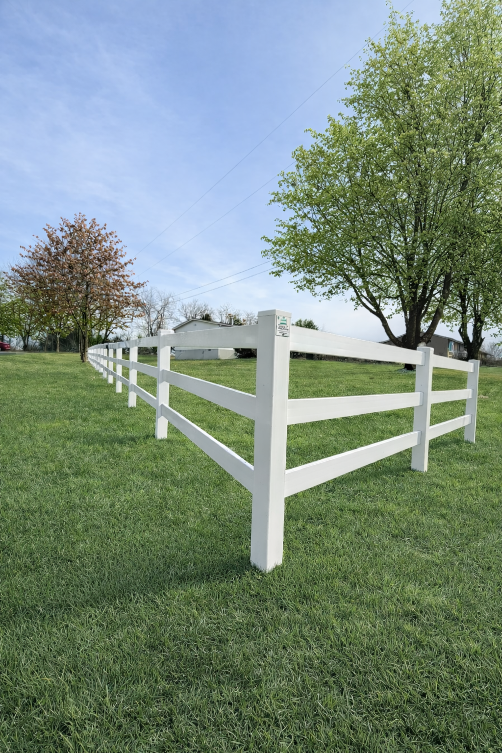 White wooden fence corner on a grassy lawn with trees and cloudy sky