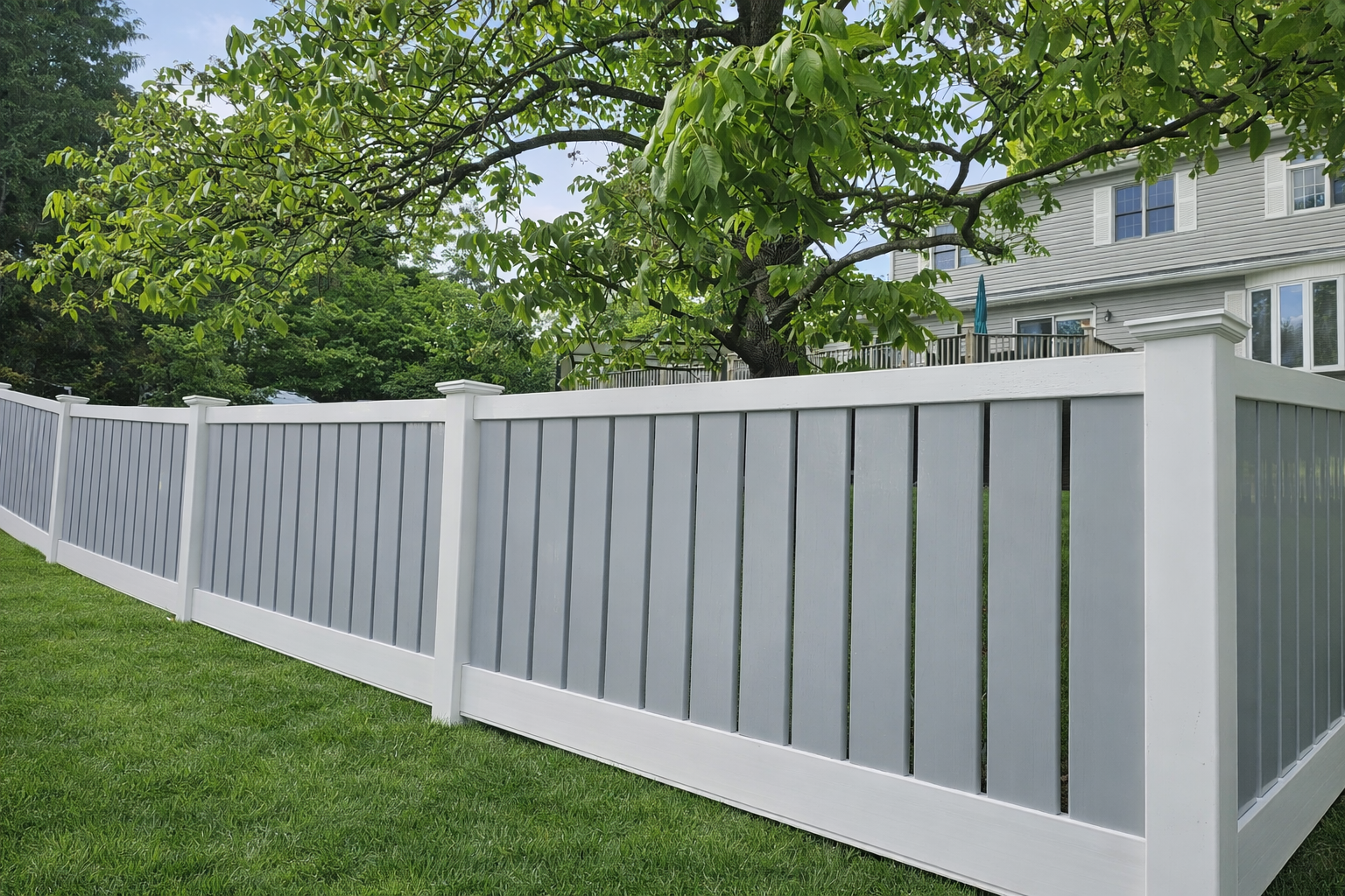White vinyl picket fence bordering a green lawn beside a house with trees in the background
