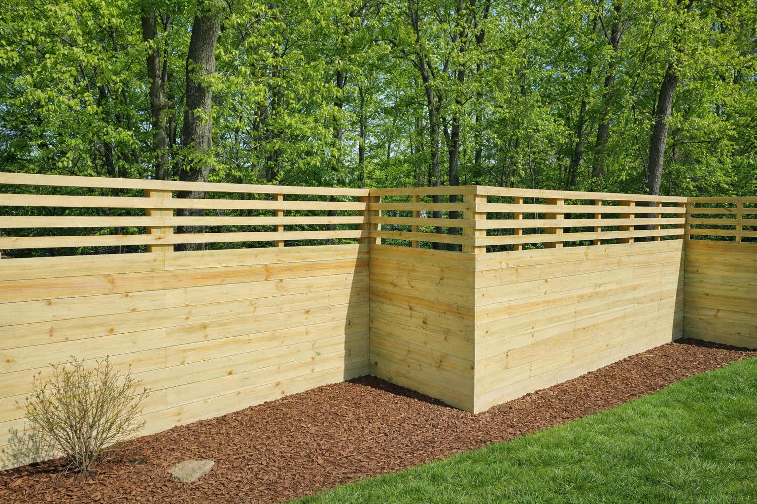 Wooden privacy fence with horizontal slats along a landscaped backyard border, backed by green trees.