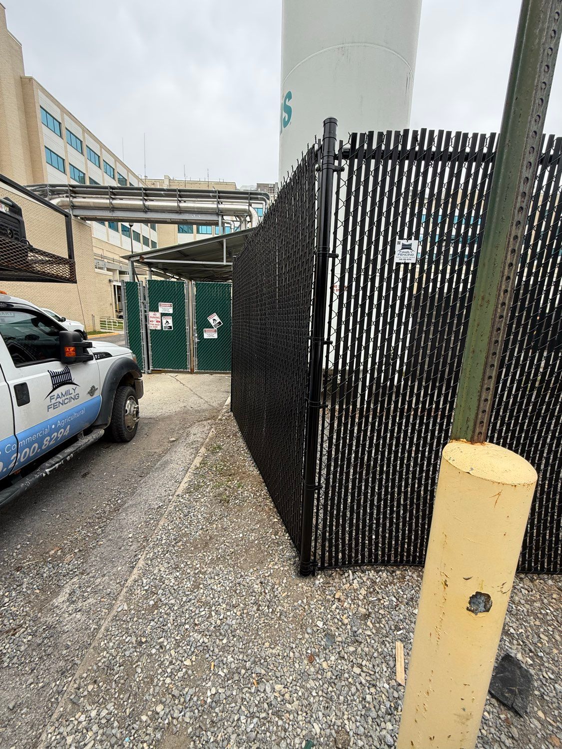 Gravel alley beside a black chain-link fence, green utility doors, and a parked police truck.
