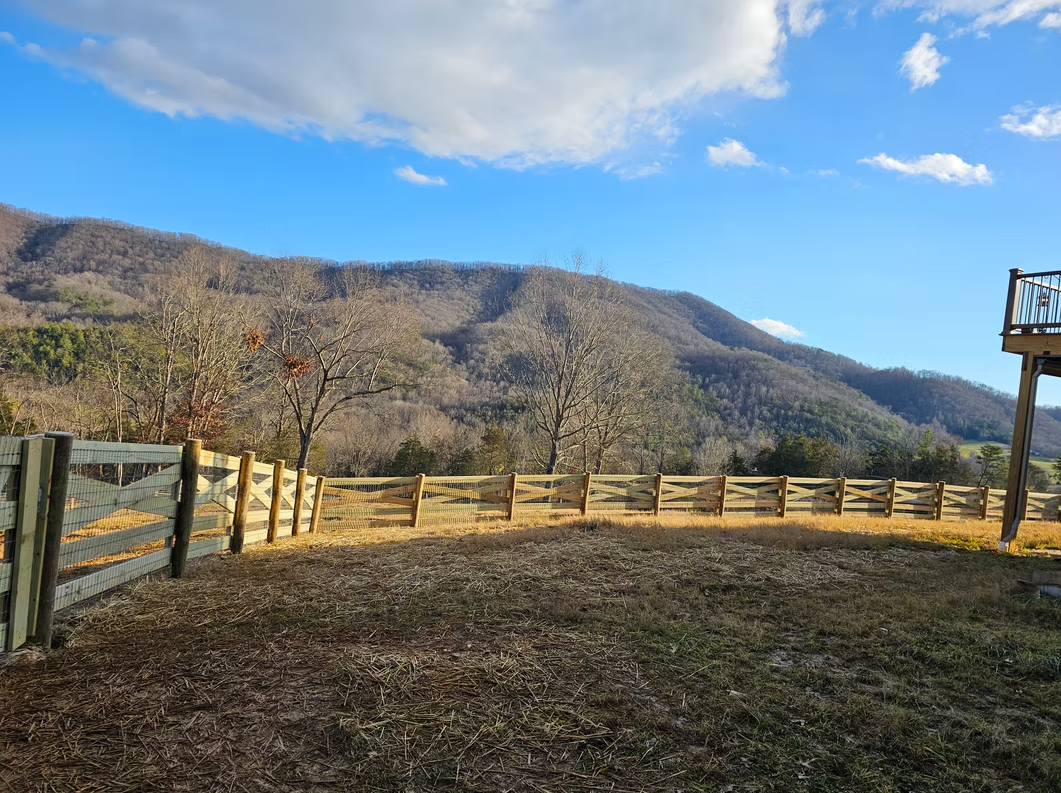 Wooden fence overlooking a mountain valley under a blue sky with scattered clouds