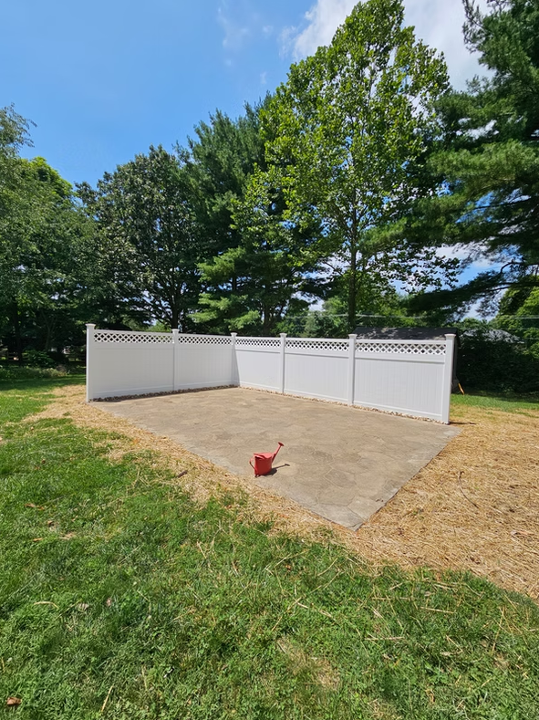 White vinyl fence panels in a grassy yard with trees and a red bucket in front