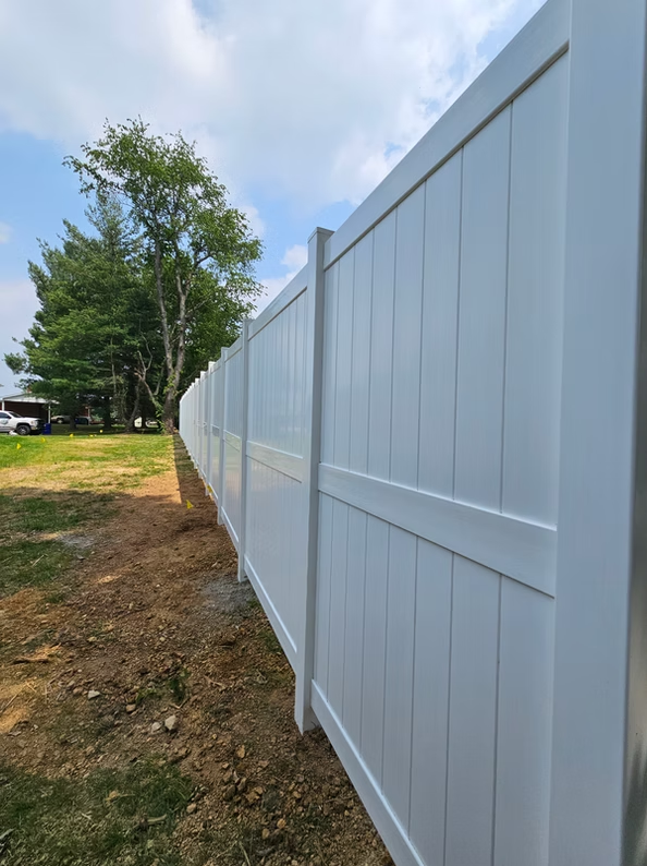 White vinyl fence along a grassy yard under a partly cloudy sky.