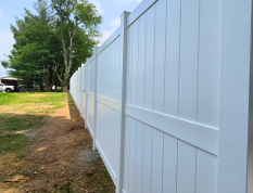 White vinyl fence along a grassy yard with trees in the background