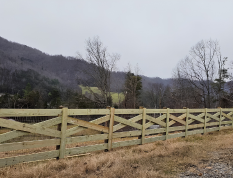 Wooden fence beside a grassy field with leafless trees and a cloudy mountain backdrop