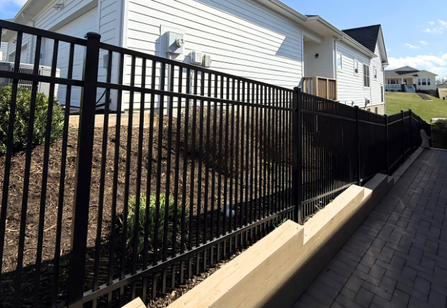 Black metal fence along a sloped walkway beside a white house in a residential neighborhood.