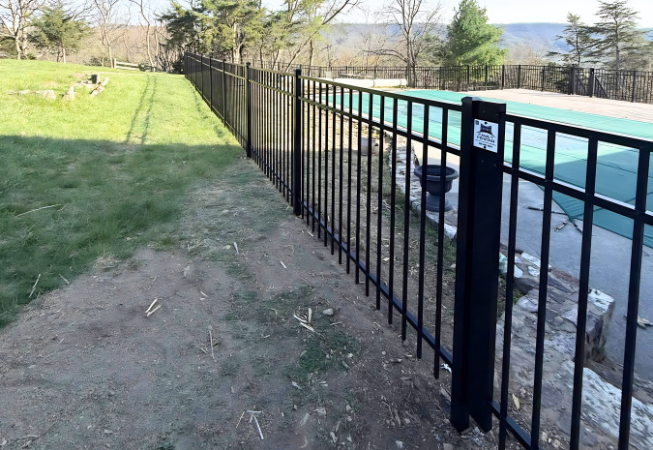 Black metal fence beside a turquoise pool, with grass and a dirt path in the foreground