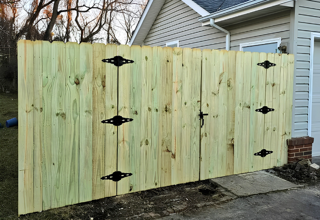 New wooden fence gate with black hinges beside a house and driveway