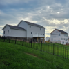 White houses on a grassy hillside behind a black fence under a cloudy sky at sunset