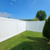White vinyl fence bordering a green lawn with a tall evergreen tree under a clear blue sky