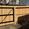 Wooden fence with a black gate in a yard on a sunny day