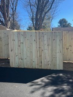 Fresh wooden fence panels along a paved area with trees and houses in the background