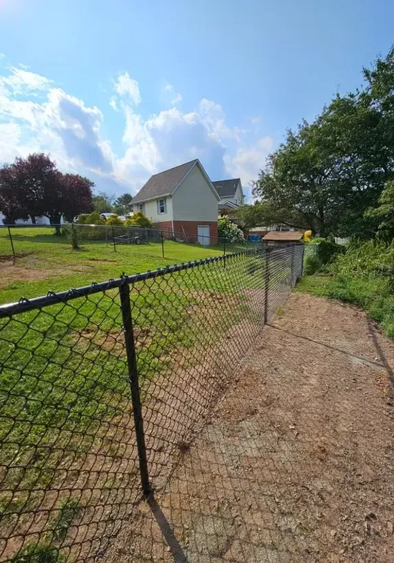 Chain-link fence overlooking a grassy yard, with a small pond and houses under a blue sky