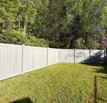 White vinyl fence along a grassy yard beside trees and a driveway