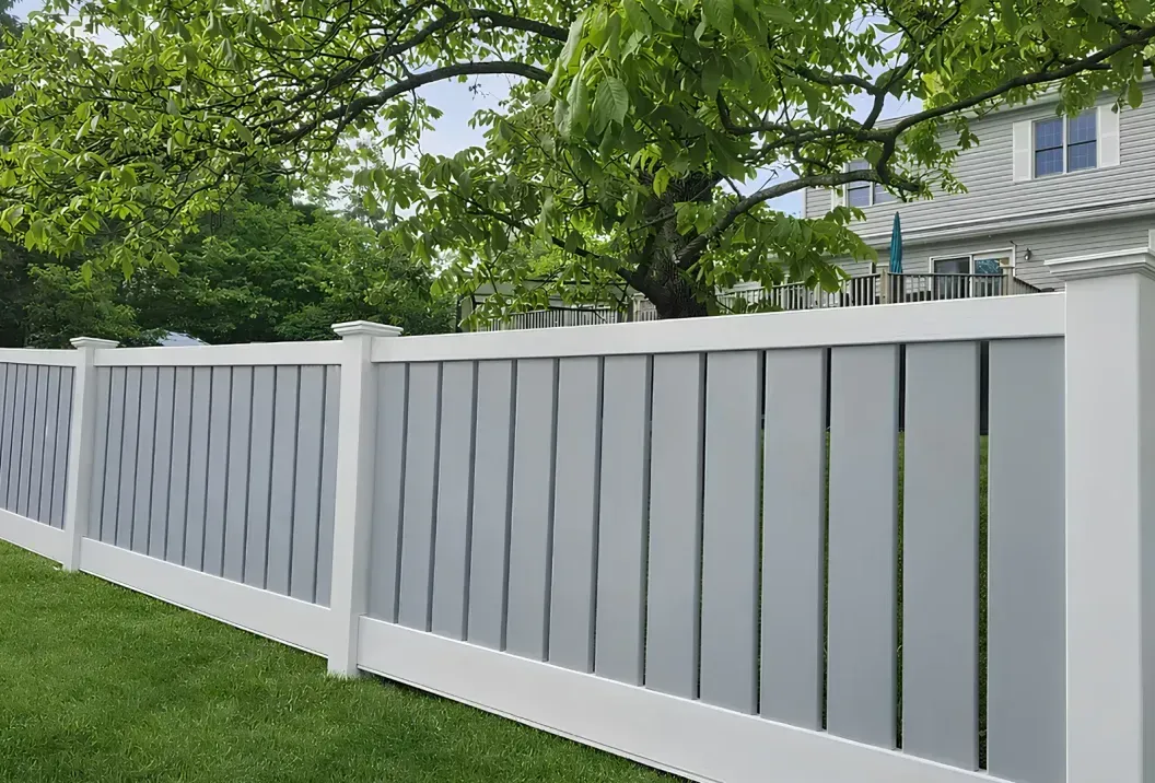 White vinyl fence along a green lawn with trees and a house in the background