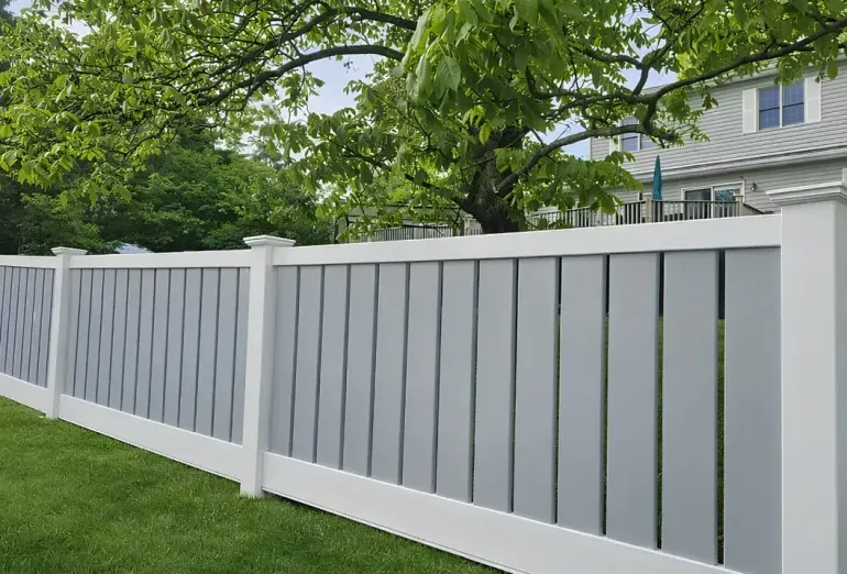 White vinyl fence along a green lawn with trees and a house in the background