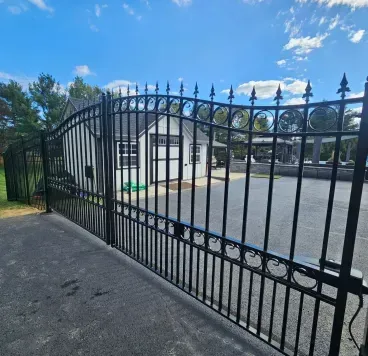 Black wrought-iron gate between stone pillars at a tree-lined driveway entrance