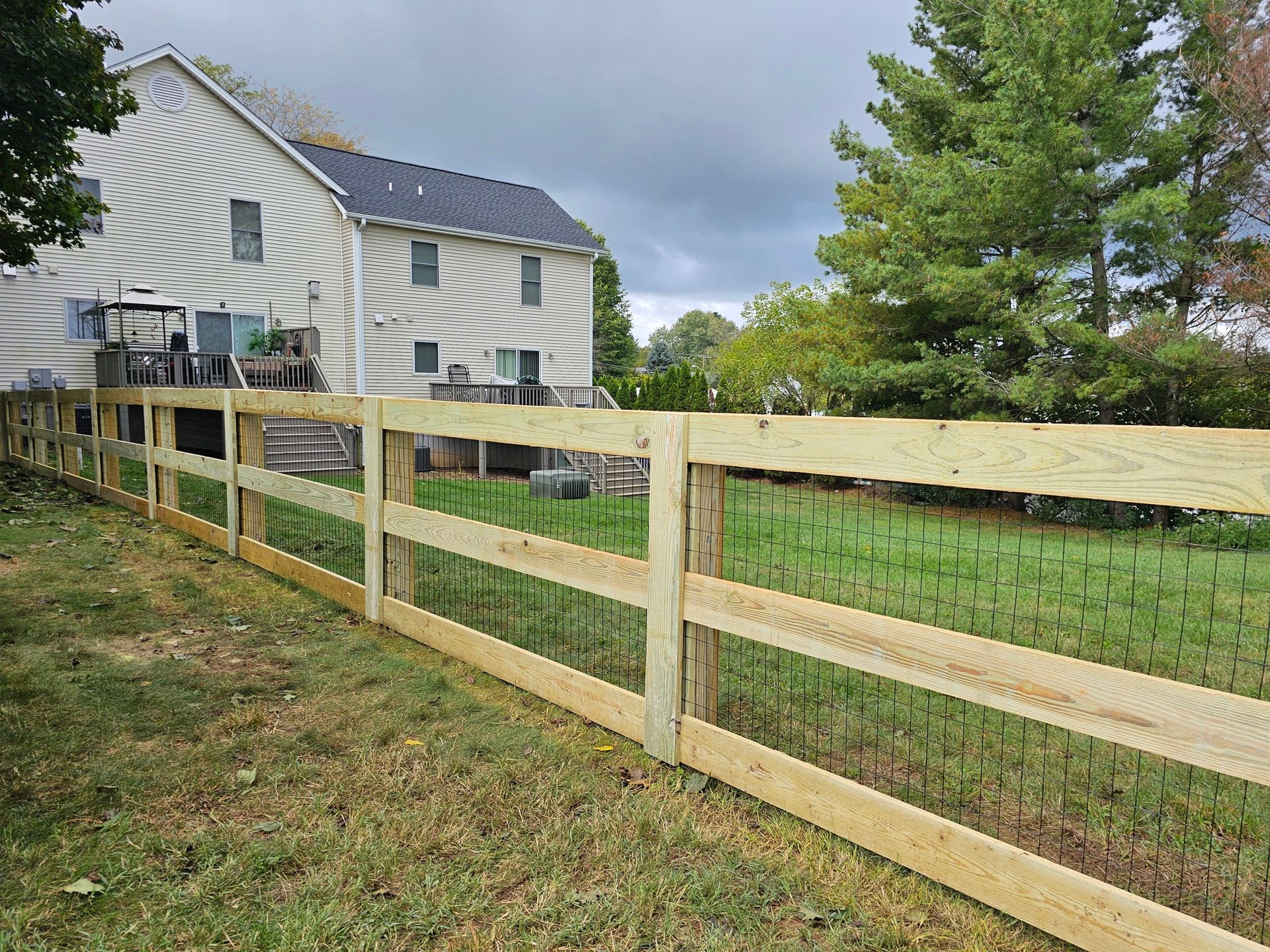 Backyard wooden fence beside a beige house and grassy yard under cloudy sky