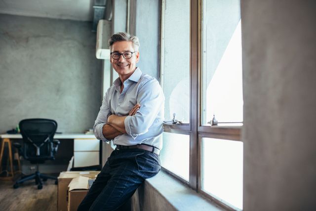 Man standing by a large window in a modern office, arms crossed and smiling