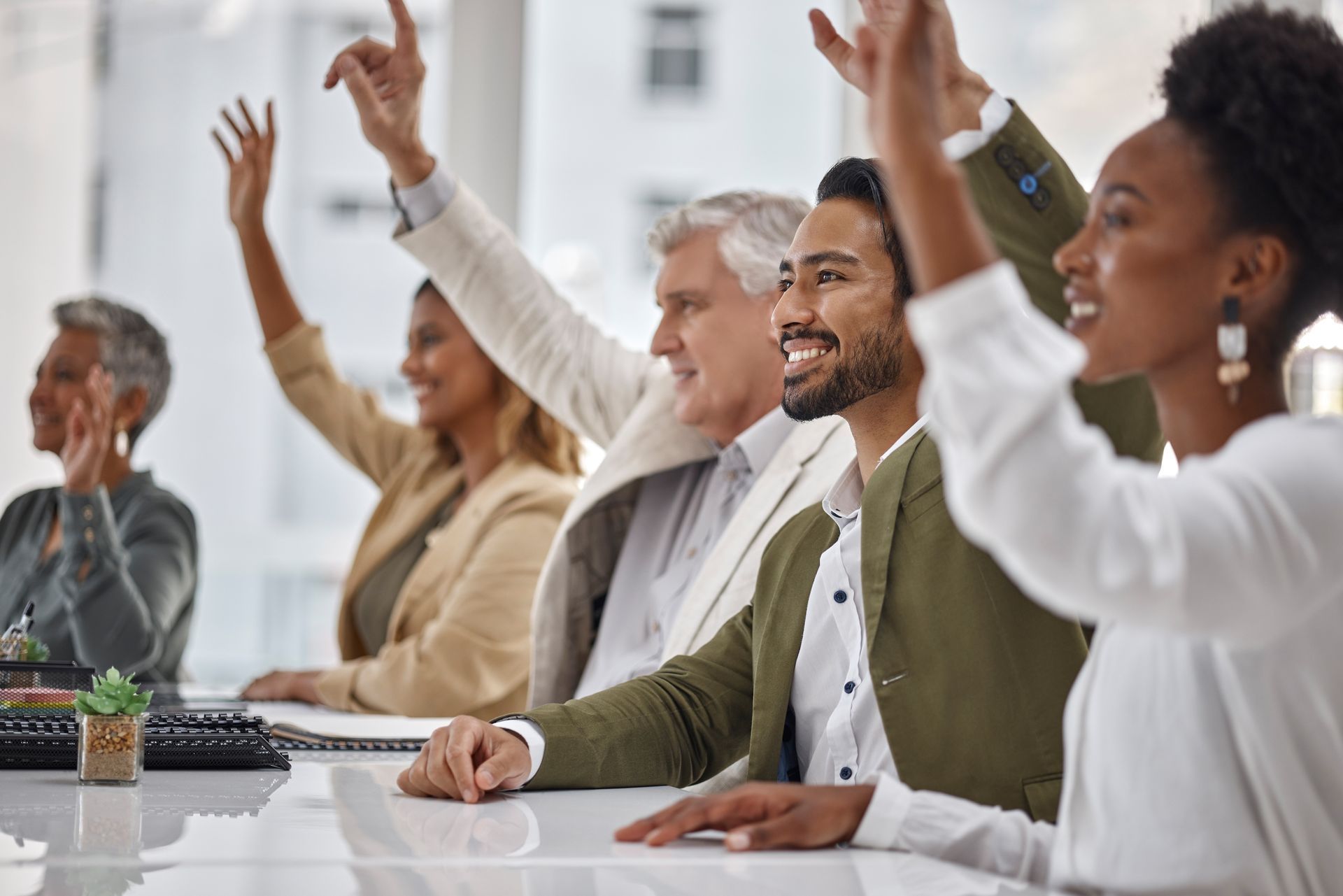 Audience members raising hands in a bright meeting room, seated at a conference table