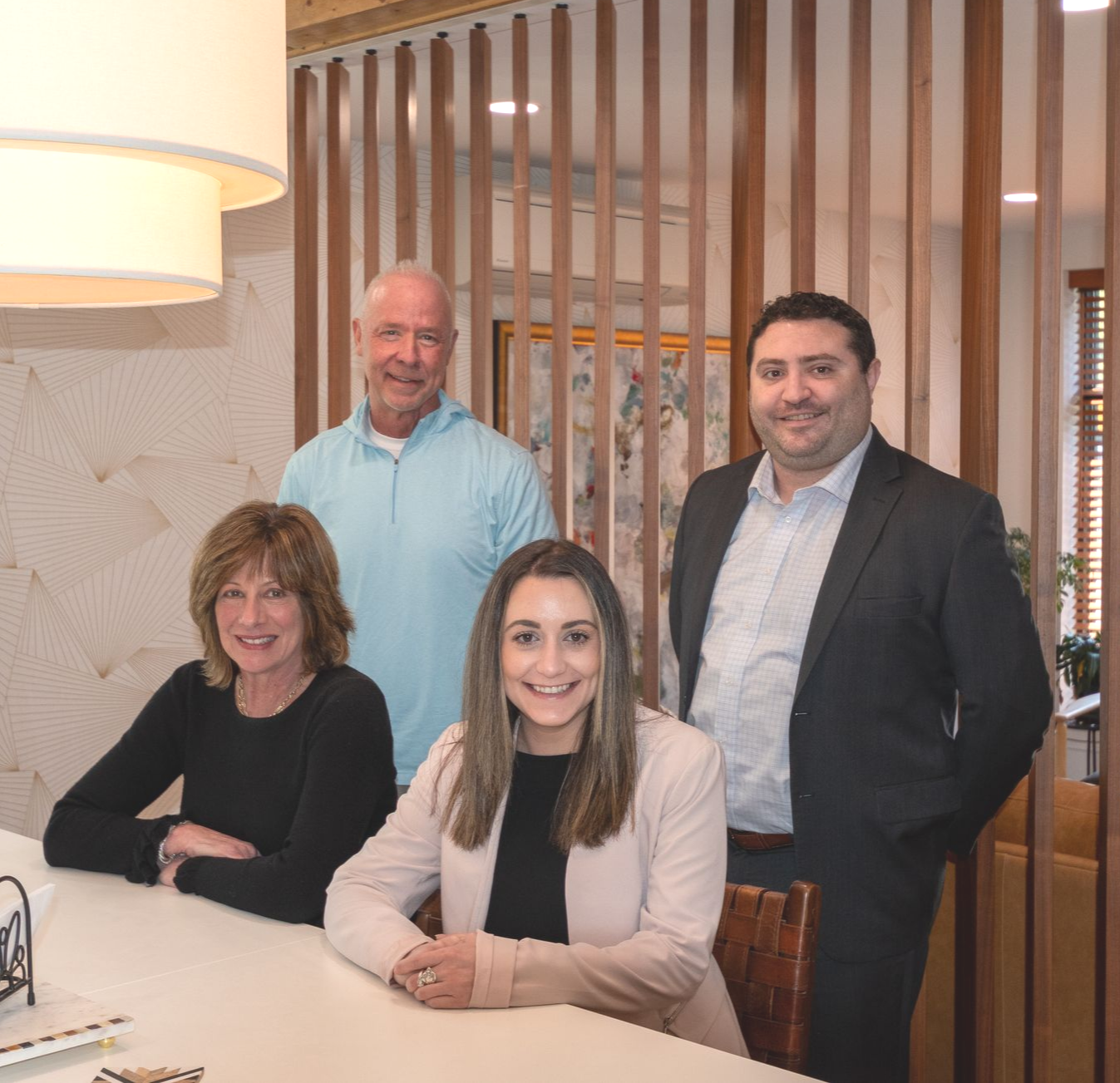 Tim Humphreys, Brent Bonstigl, Corrine Curcio and Jane Atkins of Delaware Wealth Planners. Four people posing in a modern office lounge, seated and standing behind a white table.