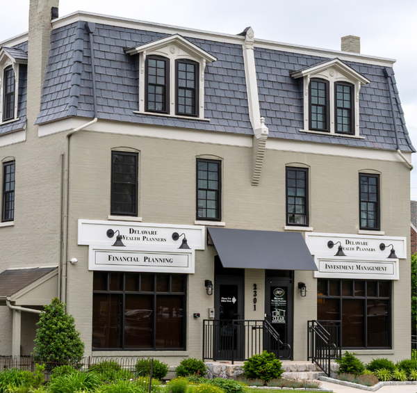 Delaware Wealth Planners two story office located in Wilmington, Delaware. Two-story cream storefront with slate roof, black awnings, and flower beds in front