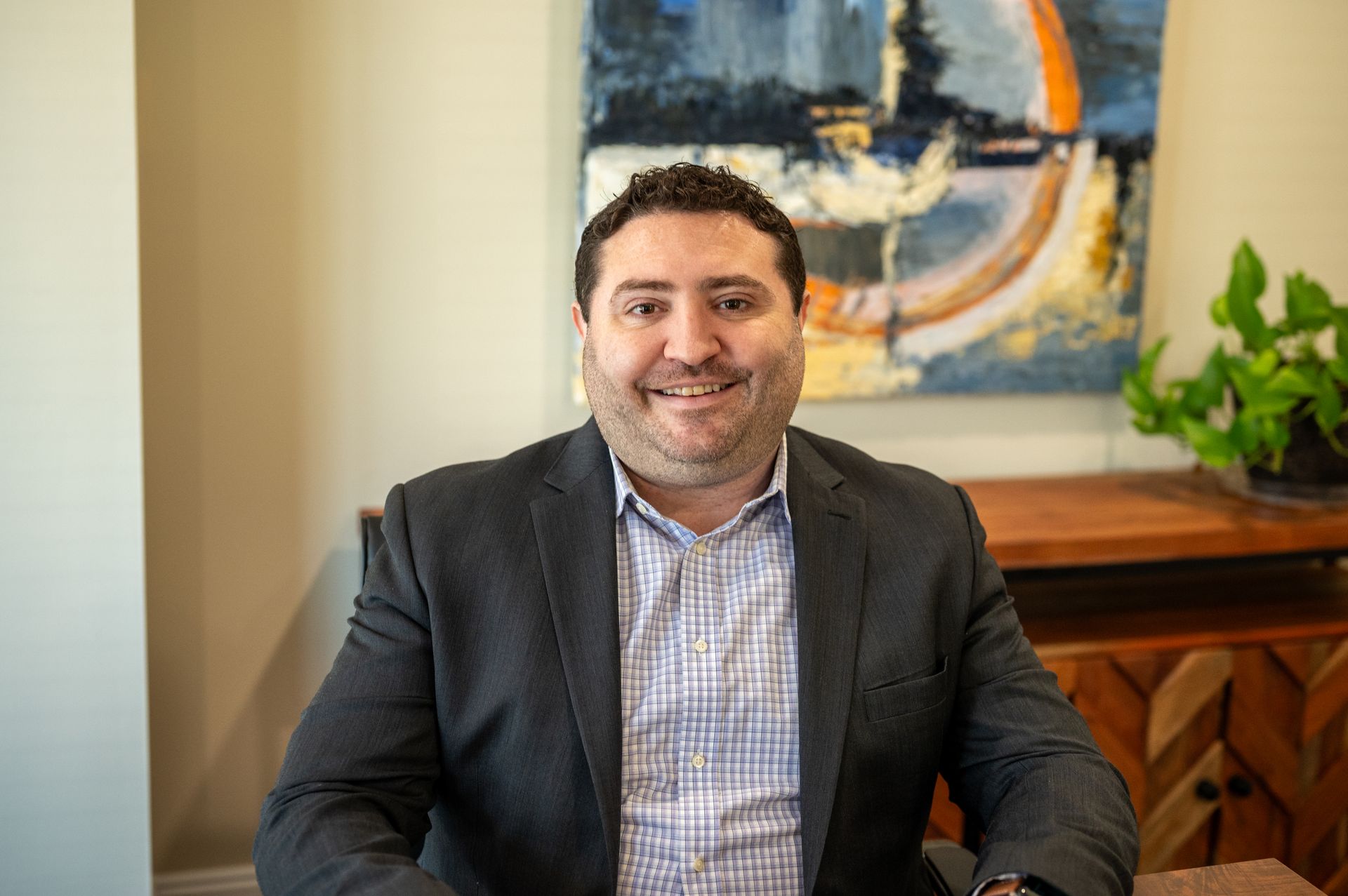Brent Bonstigl of Delaware Wealth Planners in a dark suit seated indoors, smiling in front of a colorful abstract painting and wooden cabinet